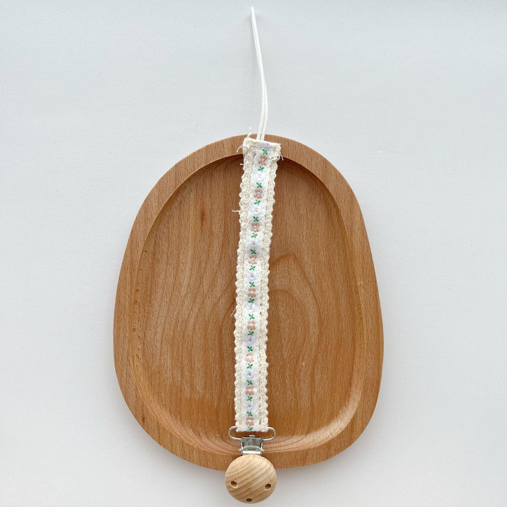 Floral Ribbon Dummy Clip, Lace Edge Soother Holder with Beech Wood Clip, 28.5 cm, 7 Designs, shown on a bed